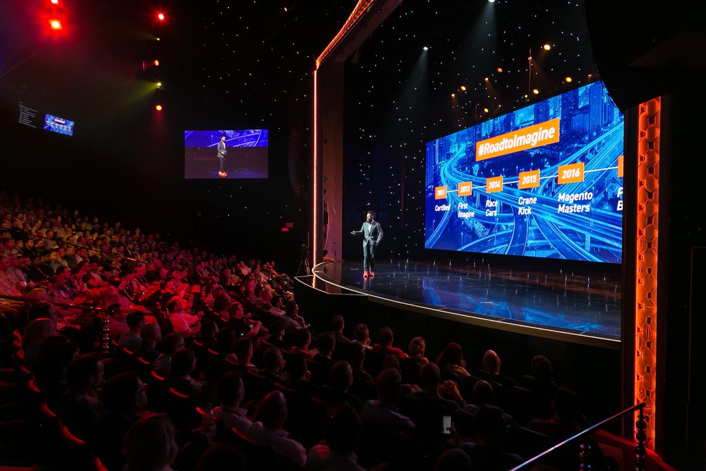 speaker presents in front of LED screens and stage lighting at ecommerce conference