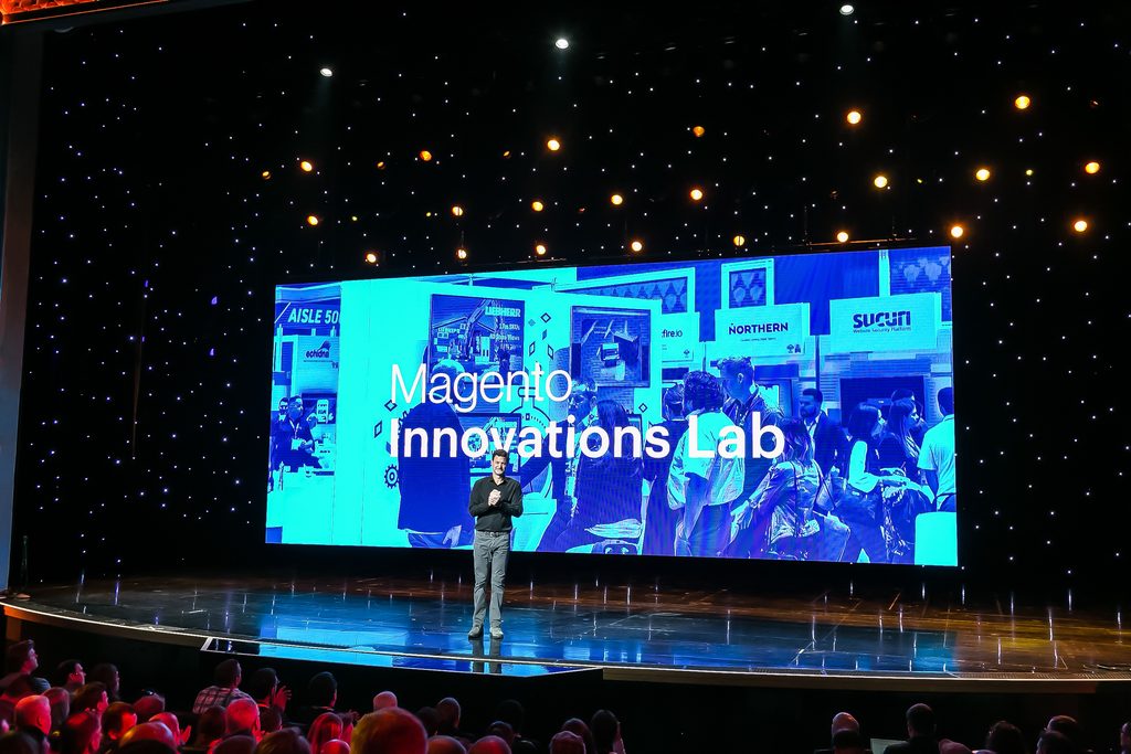 speaker presents in front of LED screens and stage lighting at ecommerce conference