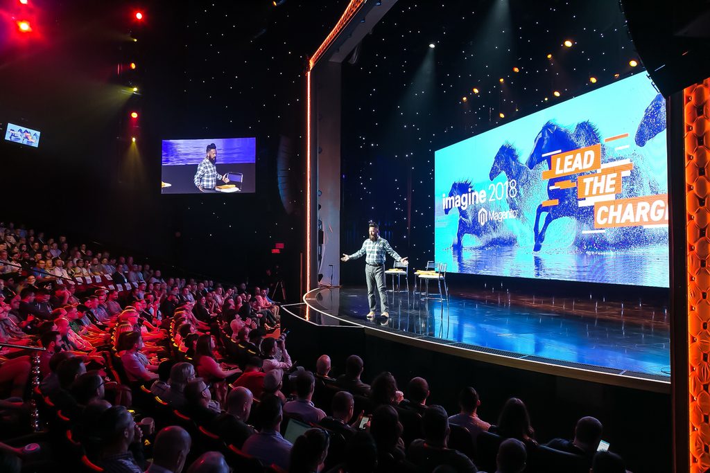 speaker presents in front of LED screens and stage lighting at ecommerce conference